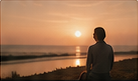 Someone sitting alone watching the sun set over water.